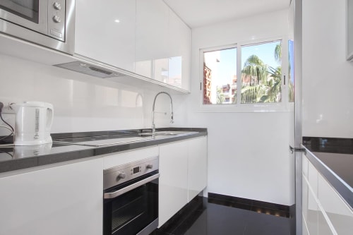 Cocina moderna blanca con encimeras oscuras, electrodomésticos de acero inoxidable y vistas al mar en apartamento de Marbella