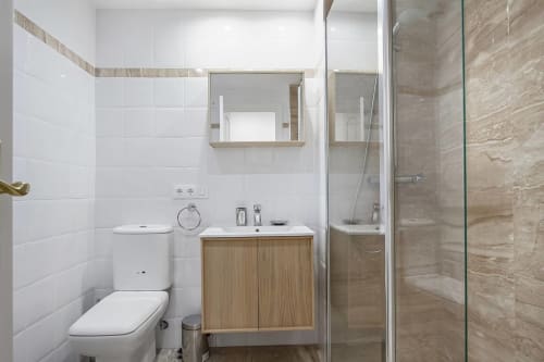 Baño moderno en apartamento SACORO Marbella con azulejos blancos, tocador de madera, espejo de medicinas y ducha walk-in
