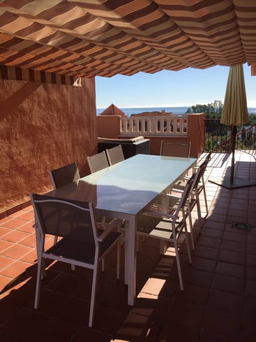 Terraza de apartamento en Marbella con mesa de comedor, toldo rayado, vistas al mar y arquitectura mediterránea