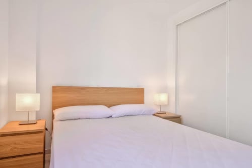 Dormitorio moderno en apartamento SACORO de Marbella con cabecero de madera, ropa de cama blanca e iluminación contemporánea