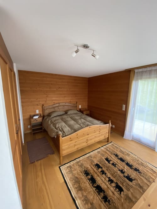 Chambre en bois à la Grangette Villars avec lit, table de nuit et tapis à motifs animaliers à Villars-sur-Ollon