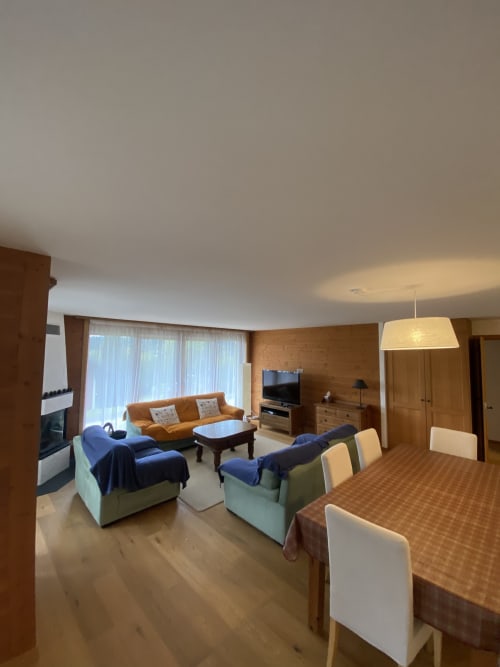 Spacieux séjour à Grangette Villars avec canapé orange, fauteuils bleus, table à manger, télévision et vue sur les montagnes