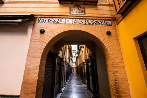 Entrada al mercado de artesanía en la Alcaicería de Granada, con arco de ladrillo y calle estrecha entre edificios históricos.