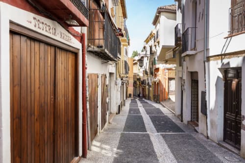 Calle empedrada en el Albaicín de Granada con fachadas blancas, puertas de madera y balcones de hierro forjado.