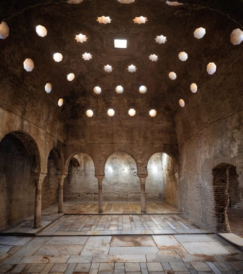 Interior de los Baños Árabes de Granada con arcos de piedra, bóveda con lucernarios estrellados y suelo de mármol.