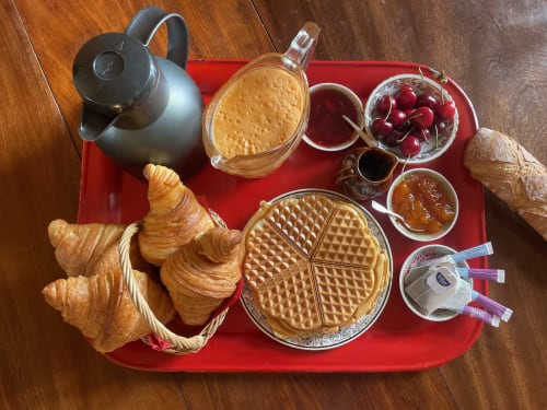 Petit-déjeuner au Château de Vaux Morvan : gaufres, croissants, beurre de cacahuète, confiture, cerises et café sur plateau rouge.