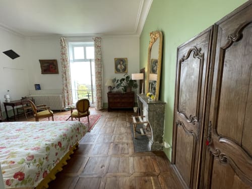 Chambre élégante au Château de Vaux Morvan avec literie fleurie, mobilier d'époque, armoire bois ornée et accents verts