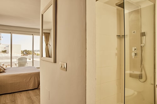 Baño lateral de la habitación Studio Sea View con ducha de cristal, azulejos color crema y vistas al balcón en hotel Formentera Especial, La
