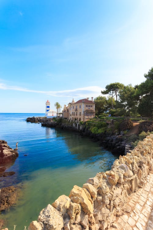 Casas de Juromenha coastal mansion with striped lighthouse, rocky cliffs and turquoise Mediterranean waters, Juromenha