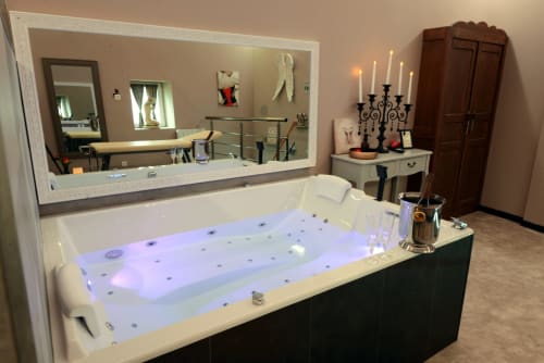 Luxurious spa bathroom with illuminated 2-person jacuzzi tub, large mirror, vanity, candelabra, and romantic amenities at Les