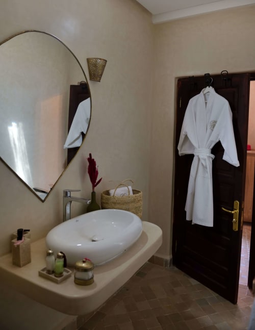 Luxe badkamer in Riad Palau Marrakech met ovaal wastafel, ovale spiegel, witte badjas en decoratieve accessoires in de Chambre
