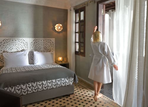 Vrouw in witte jurk die de gordijnen opent in de Chambre Royale van Riad Palau Marrakech, Marokko