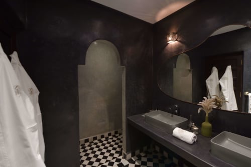 Elegant donkere badkamer in Riad Palau Marrakech met gewelfde nissen, geblokt tegelvloer, dubbele wastafels en moderne voorzieningen