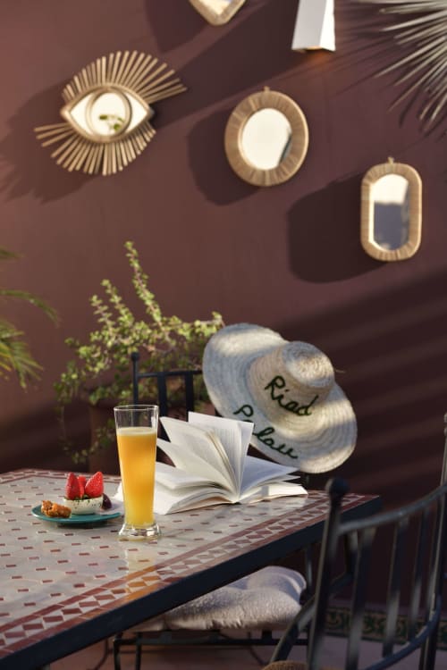 Zonnig leeshoekje in Riad Palau Marrakech met opengeslagen boek, sinaasappelsap, gebak en decoratieve hoed