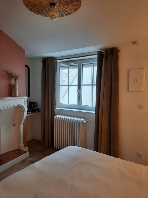 Chambre accueillante de la Maison Rinette à Dijon avec mur terracotta, grande fenêtre et radiateur classique