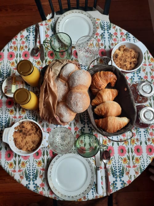 Table de petit-déjeuner à la Maison Rinette à Dijon avec viennoiseries, croissants, jus et service de café sur nappe à fleurs.