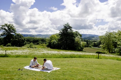 Couple picnicking on green meadow at Château de Vaux Morgan, Étang sur Arroux, with countryside and white wildflowers in