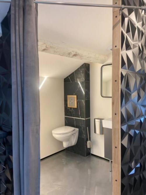 Salle de bain moderne de la villa au Domaine du haut de la Dombes avec toilettes murales et accents en marbre noir