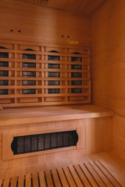 Intérieur d'un sauna en bois aux murs de cèdre, sièges en gradins et radiateur infrarouge à la villa Domaine du haut de la Dombes