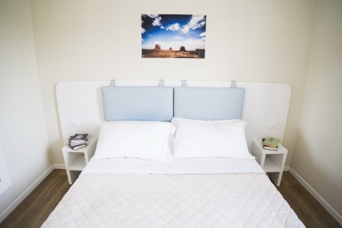 Camera moderna presso Residence Balconi del Conero con biancheria bianca, testata azzurra e quadri del paesaggio desertico