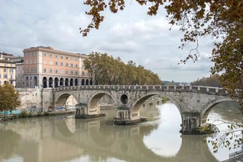 Antico ponte in pietra che attraversa il Tevere a Roma con architettura classica e fogliame autunnale