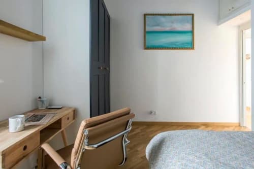 Accogliente camera da letto in appartamento romano con scrivania in legno, sedia, opera d'arte turchese e pavimenti in legno duro vicino a Campo de' Fiori