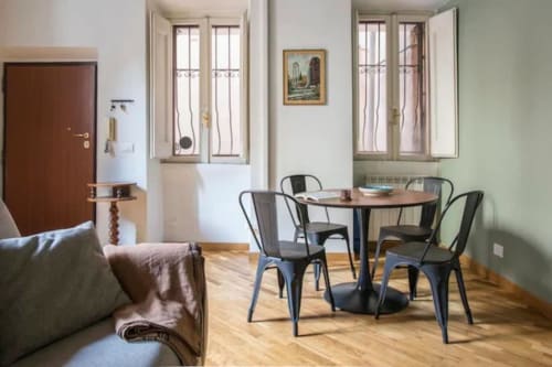 Accogliente zona pranzo in appartamento romano con tavolo rotondo, sedie in metallo, parquet, finestre e divano