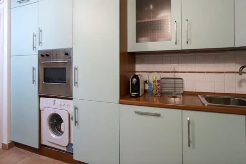 Cucina moderna in appartamento romano con armadi bianchi, forno in acciaio inox, lavatrice e piano di lavoro in legno
