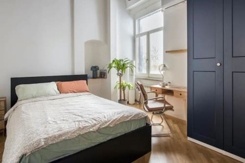 Accogliente camera da letto a Roma con letto nero, zona lavoro, luce naturale, piante e pavimento in legno vicino a Campo de' Fiori