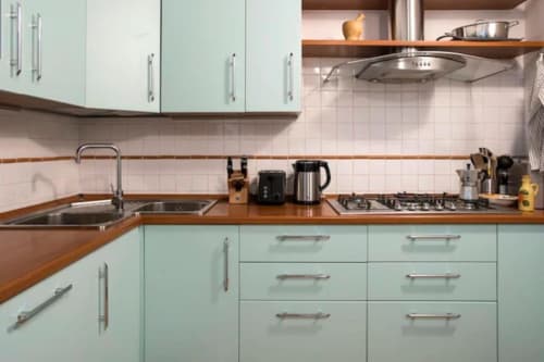 Cucina moderna verde menta con piano in legno, elettrodomestici in acciaio inox, piano cottura a gas e rivestimento in piastrelle bianche a Roma