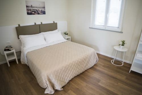 Studio apartment bedroom at Residence Balconi del Conero with queen bed, white nightstands, wooden flooring, and sea view