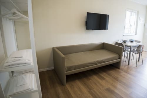 Modern studio apartment living area with beige sofa, wall-mounted TV, wooden flooring, and dining table at Residence Balconi