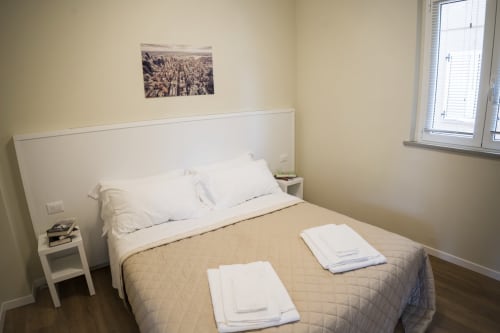 Camera da letto luminosa con letto queen size, cuscini bianchi, asciugamani e finestra sulla corte interna