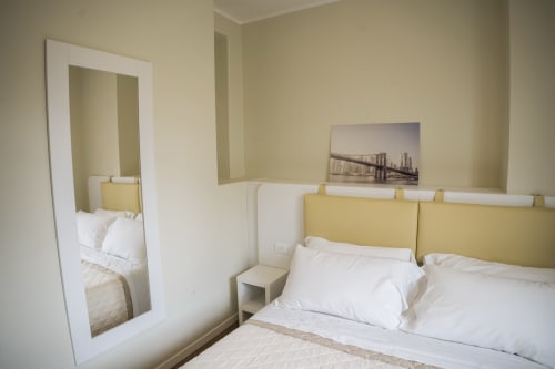 Modern bedroom at Residence Balconi del Conero with yellow headboard, white bedding, mirror, and cityscape artwork