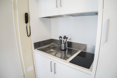 Compact kitchenette with induction cooktop, sink, storage cabinets, and utensil holder at Residence Balconi del Conero