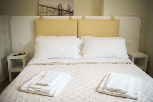 Modern bedroom at Residence Balconi del Conero with yellow headboards, white pillows, and folded towels on quilted bedding