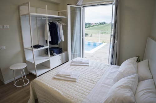 Bright bedroom with pool view at Residence Balconi del Conero, featuring white wardrobe, bed with linens, and terrace access