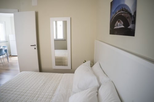 Modern bedroom in Residence Balconi del Conero apartment with white bedding, mirror door, and shark artwork on beige walls.