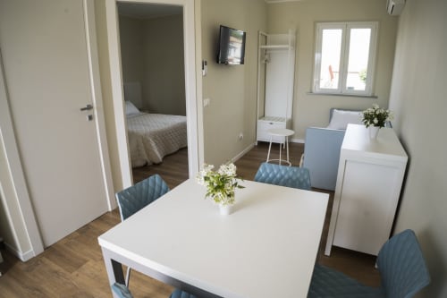 Modern apartment living area with white dining table, blue chairs, and bedroom entrance at Residence Balconi del Conero,