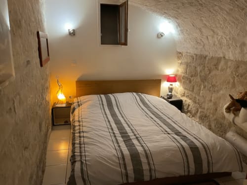 Chambre douillette chez Adrien Paris avec literie rayée, murs de pierre, éclairage chaleureux et lampes de chevet