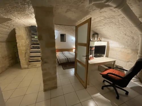 Chambre souterraine de Chez Adrien Paris avec murs en pierre, lit, bureau et chaise en sous-sol