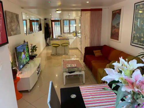 Séjour contemporain chez Chez Adrien Paris avec canapé rouge, télévision, cuisine et fleurs fraîches