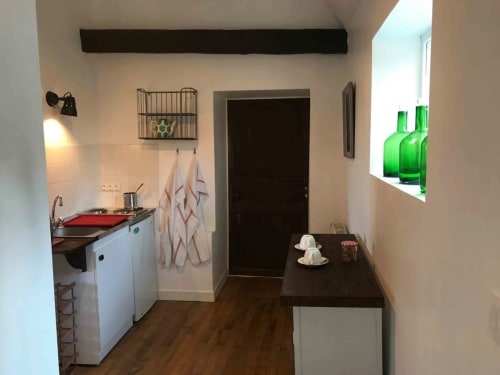 Kitchenette compacte de l'appartement Bergamote au Manoir De Rieuzal, Loubressac avec placards blancs, cuisinière rouge et coin repas
