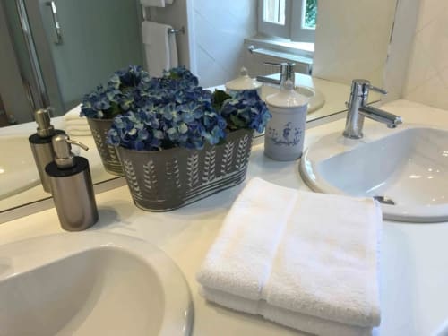 Salle de bain élégante au Manoir De Rieuzal : vasque double, serviettes blanches, hortensias bleus et accessoires à Loubressac