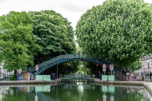Pont voûté bleu enjambant le Canal Saint-Martin avec des arbres d'un vert luxuriant à Paris
