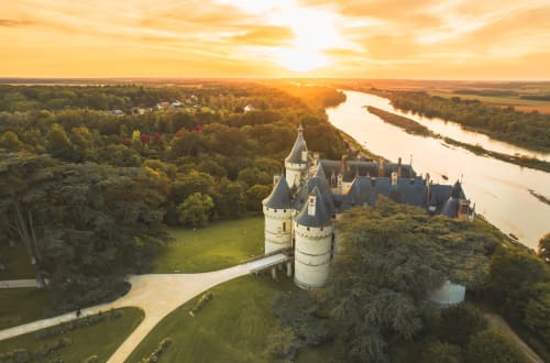 Château de Touraine au coucher de soleil surplombant la Loire, entouré de forêts luxuriantes et pelouses verdoyantes