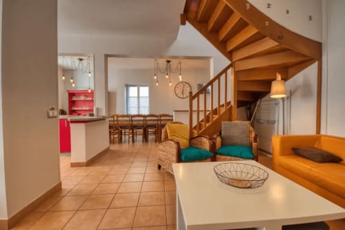 Spacieux séjour ouvert à Vacances en Touraine avec escalier hélicoïdal en bois, canapé orange et cuisine rouge.