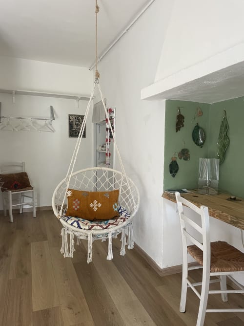 Cozy bedroom at La Cascina di Bea with hanging macramé chair, white walls, green accent wall with cookware, wooden flooring,