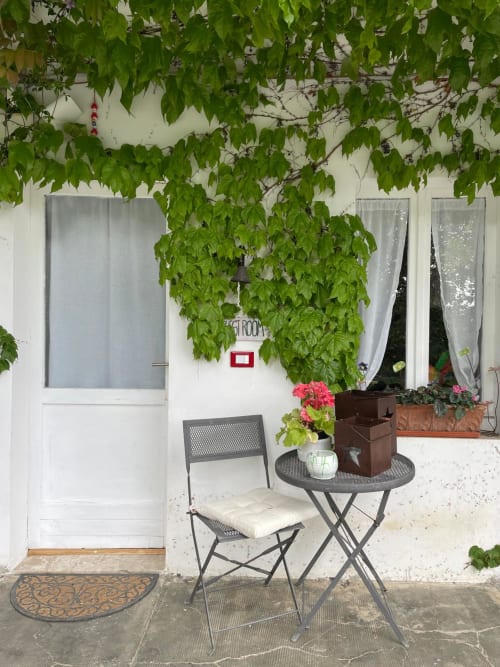 Wisteria room garden seating area with ivy-covered wall, chair, table and pink flowers at La Cascina di Bea, Bergamo