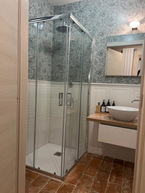 Modern bathroom at La Cascina di Bea with glass shower enclosure, white basin sink, and floral wallpaper in Iris Double Room,